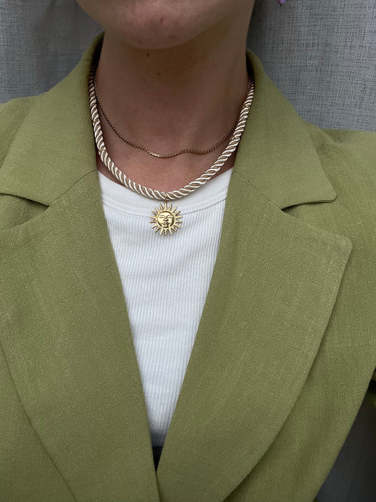 Twisted ketting beige met gouden zon bedel details groen colbert en gouden ketting
